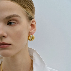 Macro view of polished 18k gold earrings with white crystals on female model