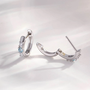 Silver drop earrings with light blue and clear zircons on a white fabric background