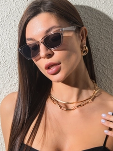 Detail of transparent grey cat eye sunglasses with gold chain necklace on a model