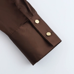 Détail de la manche d'une chemise en satin marron avec boutons dorés élégants