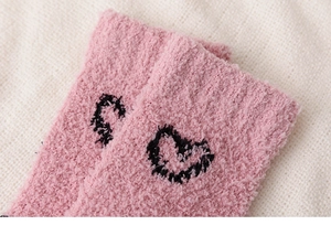 Close-up of pink coral fleece socks featuring embroidered black heart and number details
