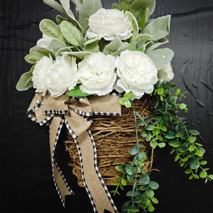 Close-up of white silk peonies and green leaves in a woven basket with a plaid bow