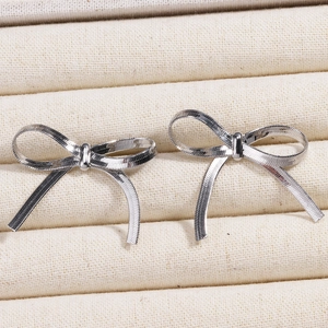 Macro shot of silver bow earrings with textured snake chain on beige fabric surface