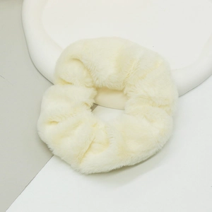 Détail d'un chouchou en fausse fourrure crème douce sur un plateau décoratif blanc