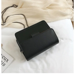 Detail of black leather texture and bronze metal chain on a minimalist square bag