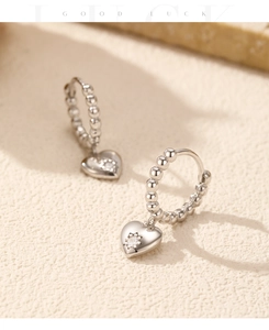 Macro detail of silver heart charm hoop earrings with crystal on textured stone base