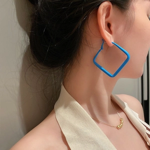 Close-up of a model wearing square Klein blue earrings and a gold beaded necklace
