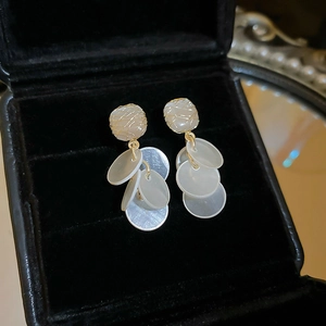 Close-up of golden shell tassel earrings with white opal stones in a luxury gift box