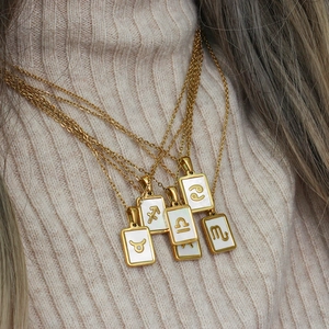 Detail of layered gold shell necklaces featuring engraved zodiac symbols for women
