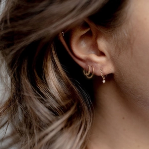 Detail of model wearing layered gold 925 silver hoop earrings with a star zircon charm