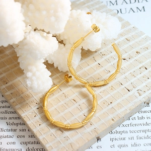 Gold-plated C-shaped earrings with bamboo texture displayed on decorative white coral