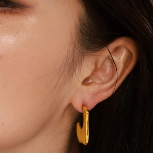 Irregular textured C-shaped 18K gold plated earrings worn by a model in a profile shot