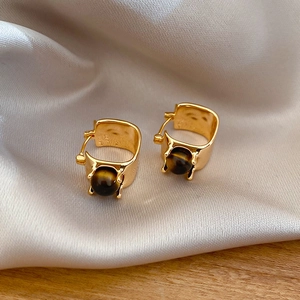 Macro view of gold-plated tiger eye earrings on silk background with soft lighting