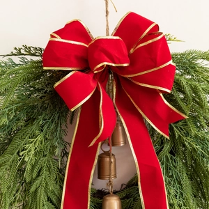 Christmas wreath with a large red velvet bow, pine needles and bronze bells on cream wall