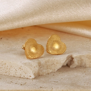 Macro shot of gold heart stud earrings with radial texture on a silk and stone background