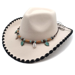 Detail of beige felt cowboy hat featuring ethnic beads and a metallic leaf pendant