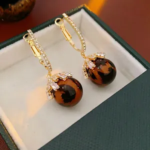 Elegant gold drop earrings with leopard-patterned spheres and zircon inlay details