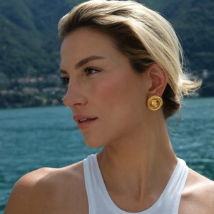 Outdoor close-up of a model wearing gold-plated spiral texture hoop earrings by a lake