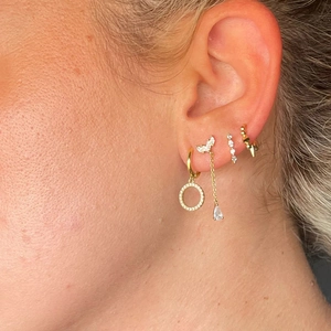 Macro shot of layered gold earrings set with sparkling crystals on model ear