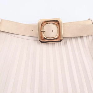 Détail de la taille d'une jupe plissée beige avec ceinture en daim et boucle dorée
