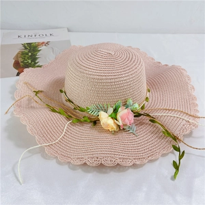 Close-up of pink woven straw hat with floral accents and wavy brim for sun protection