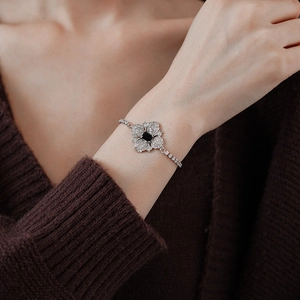 Close-up of silver bracelet featuring a black square gem and diamond-set flower petals