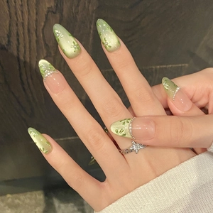 Detail of almond green cat-eye press-on nails with floral art and pearl accents