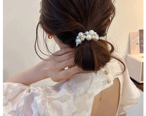 Detailansicht eines eleganten Perlenhaargummis, der einen strukturierten Haarknoten stylt