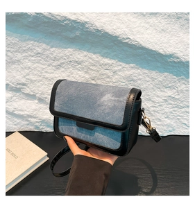Detail of blue denim and black leather stitching on a compact square crossbody bag