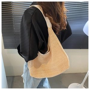 Detail of a beige woven straw shoulder bag with a wide white strap shown on a model