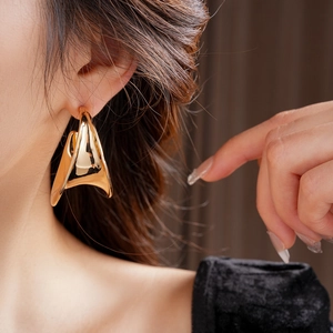 Close-up of oversized gold sculptural C-shaped earring with artistic metallic texture