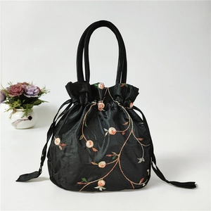 Detail of floral embroidery and drawstring closure on a black ethnic satin handbag