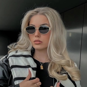 Oval metal sunglasses with gold frames and dark lenses worn by a model in black jacket