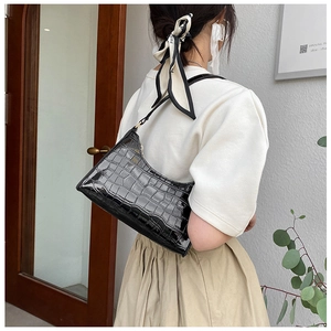 Chic black crocodile embossed patent leather baguette bag worn as an underarm shoulder bag
