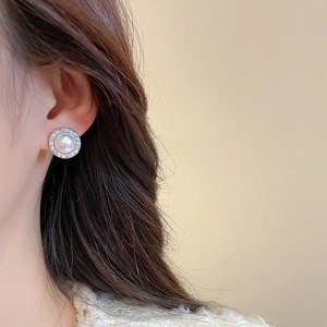 Close-up of a silver pearl earring with a zircon halo worn on a model's ear