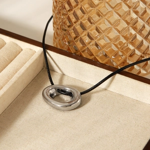 Close-up of a silver polished oval pendant with black cord in a wooden jewelry box
