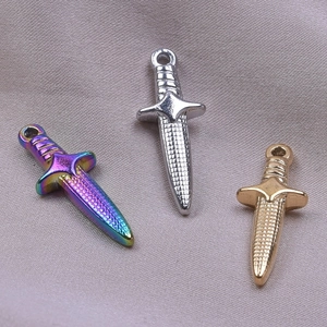 Dettaglio di tre ciondoli a spada in acciaio inossidabile nei colori arcobaleno, argento e oro