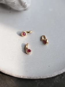 Close-up of red zircon gold-plated pendants on a white ceramic tray with soft lighting