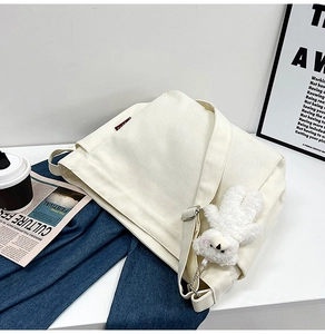 Close-up of beige canvas tote bag with a cute plush bear pendant and adjustable strap