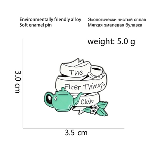 Detail of The Finer Things Club enamel pin with teapot and ribbon in mint green and white