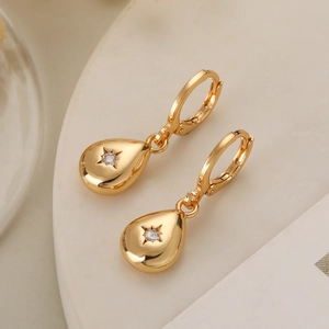 Boucles d'oreilles goutte dorées avec zircon étoilé sur un plateau en pierre