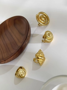Detail view of four gold spiral and seashell rings on a rustic wooden tray setup
