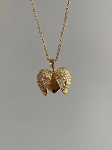 Detail of opening angel wing heart pendant with sparkling crystals on gold chain