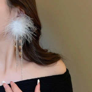 Close-up of elegant long white feather and rhinestone tassel earrings on a female model