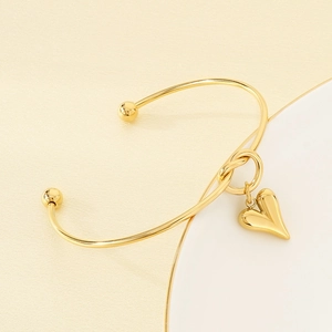 Detailed close-up of a golden knot bangle featuring a stylish heart-shaped charm pendant