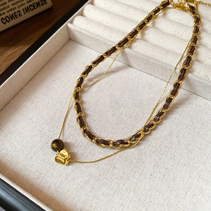 Detail of 18K gold double layer necklace with braided leather chain and tiger eye pendant