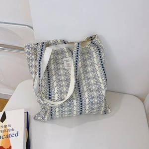 Detail of off-white canvas tote bag featuring navy floral lace patterns and woven label