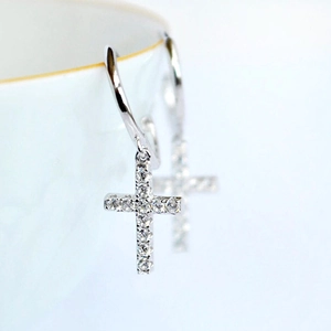 Close-up of silver hoop earrings with zircon-studded crosses on a white ceramic rim