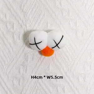 Détail macro d'accessoire en peluche avec yeux en X et nez orange, taille 4 cm par 5,5 cm