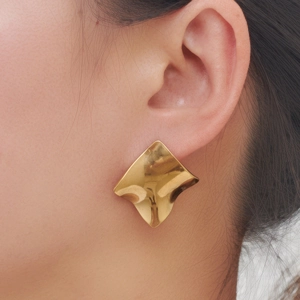 Nahaufnahme goldener unregelmäßiger geometrischer Ohrstecker mit poliertem Wellen-Finish